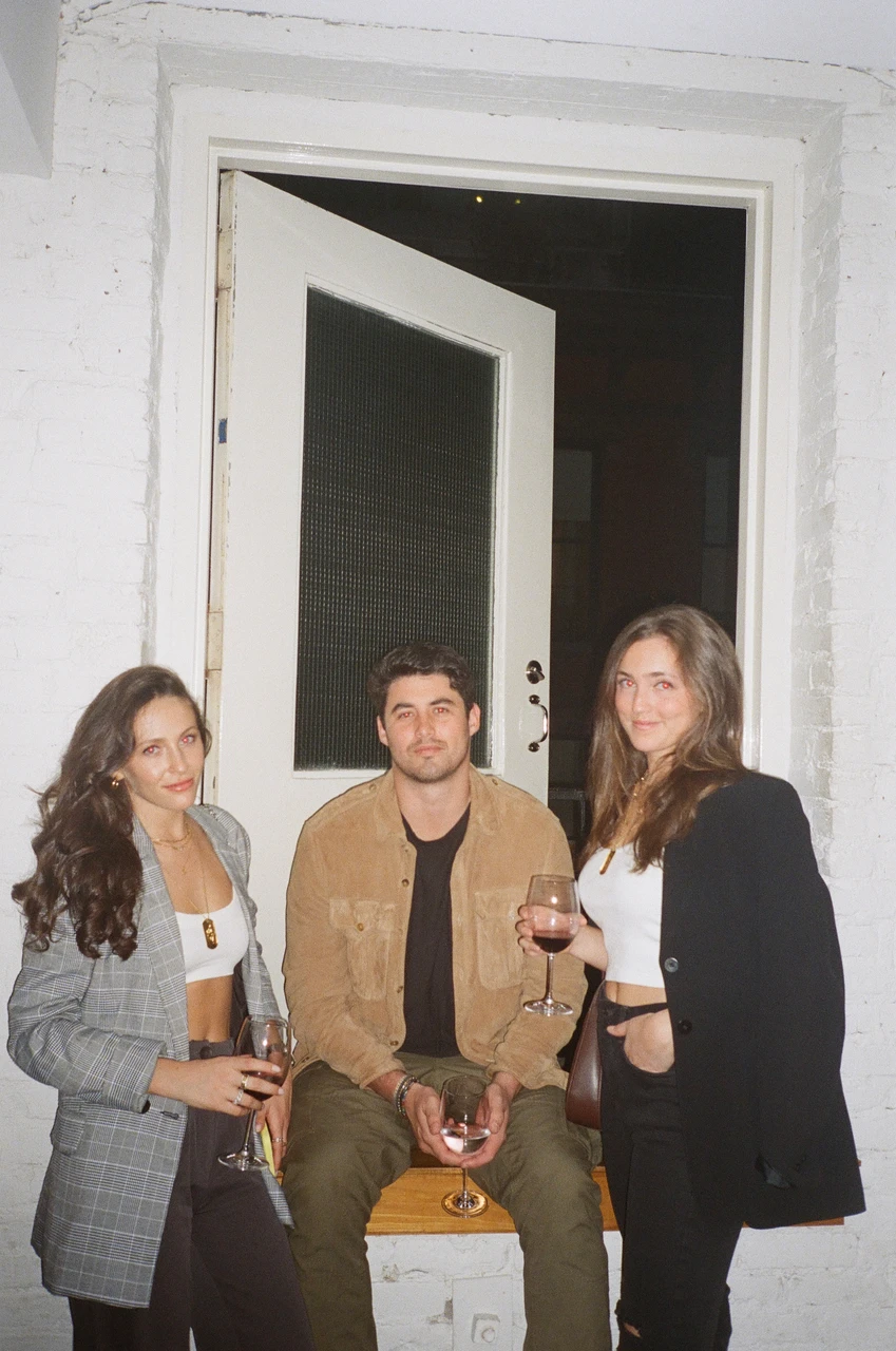 Three guests posing with drinks beside an open doorway.