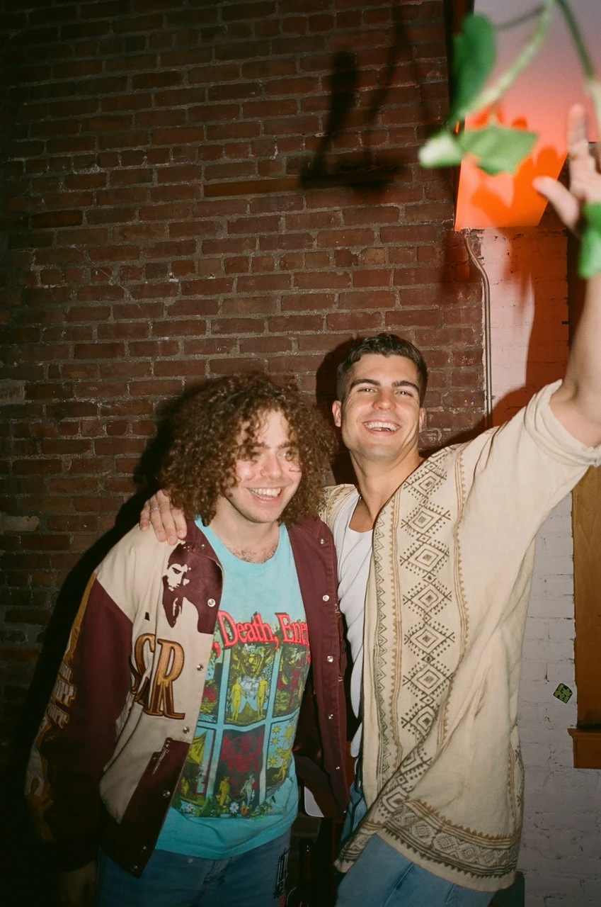 Two smiling guests posing beside a brick wall.