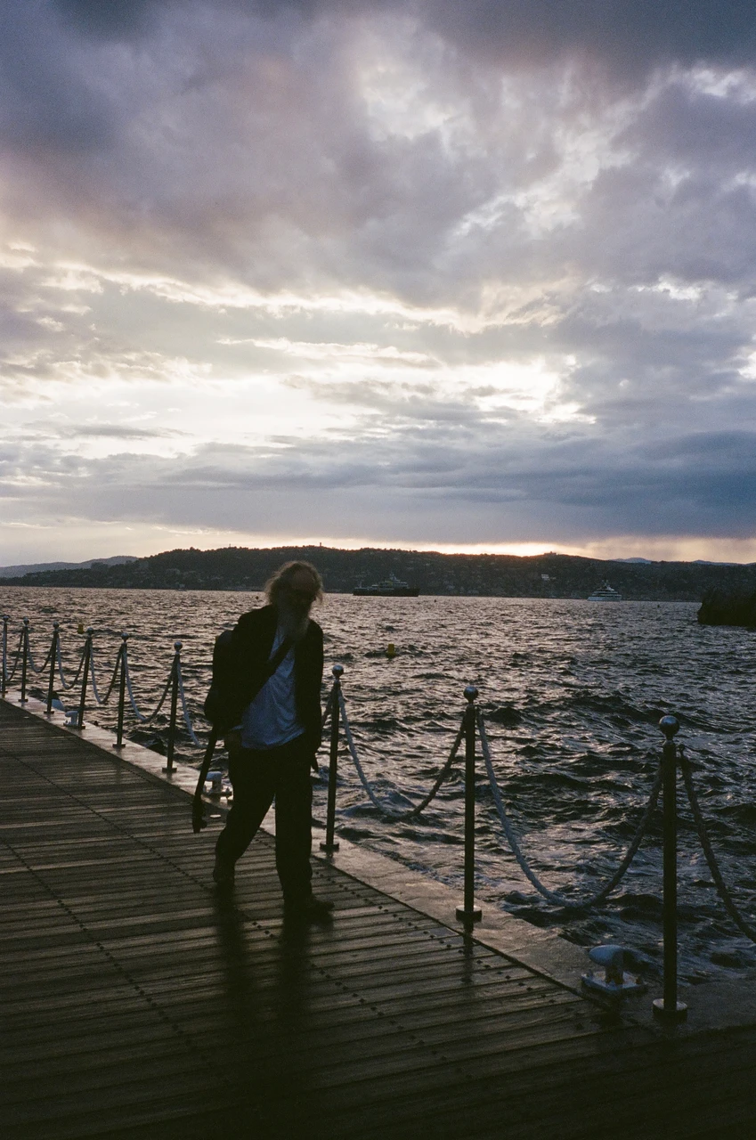 A person standing on a wooden pier beside the sea at dusk.