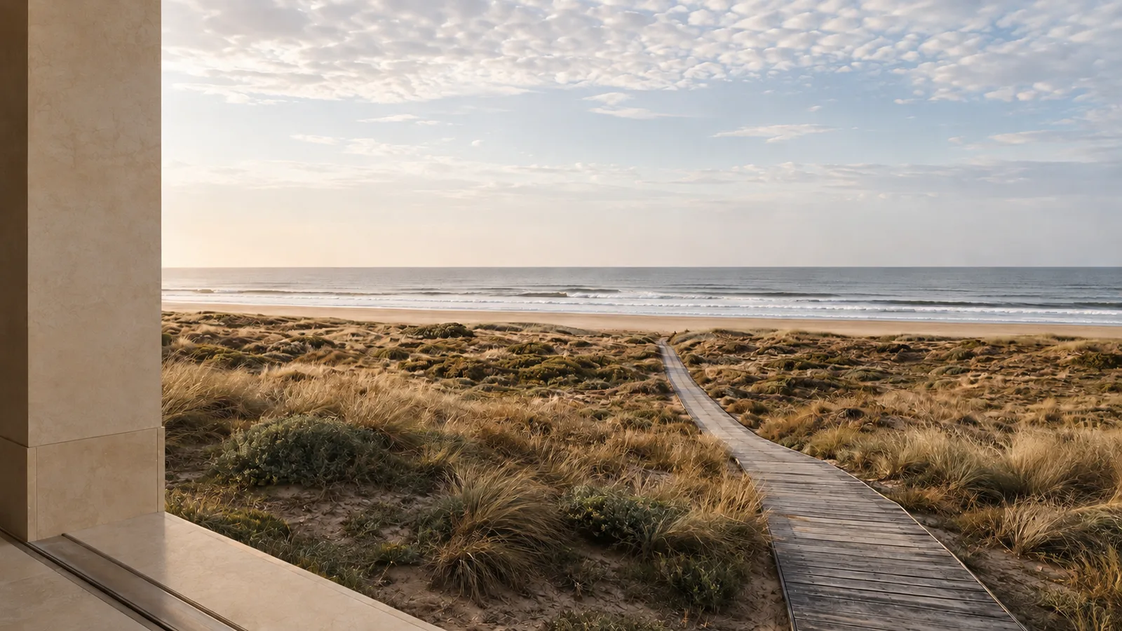 View from a stone portico across dune grass and a wooden boardwalk to the sea.